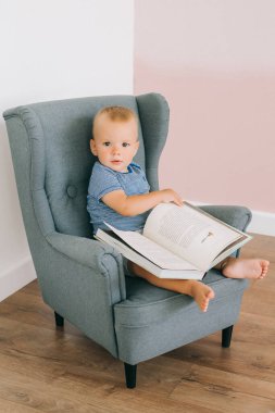 Küçük bir sandalyede oturan ve kitabını okuyan bir çocuk.