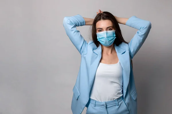 Gri arka planda izole edilmiş mavi takım elbiseli, maske takan genç bir kadının moda portresi..