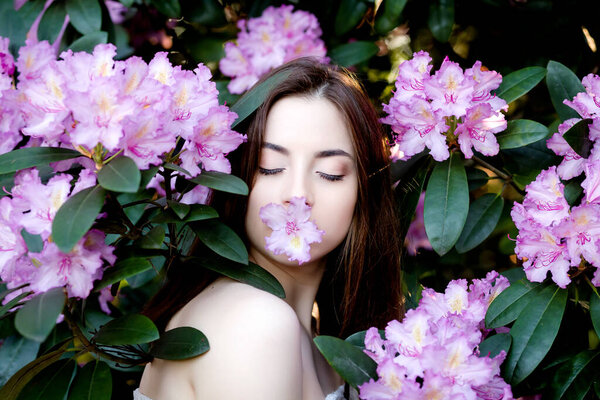 Portrait of an Asian girl, eyes closed, posing in flowers, in a spring garden, holding a lilac flower with her lips against the background of a flowering Bush . Shes calm .She sees the dreams.
