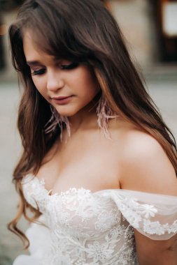 Gelin hareket halinde, omuz manzarası ve gelinlik ve aksesuarların ayrıntıları. Gözleri yere eğik, narin bir portre.