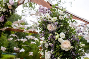 Tören için ahşap kemer, çiçekler, yeşillik, beyaz kuşlar ve mumlarla süslenmiş. Şirin, şık bir düğün süsü. Çiçek düzenlemelerine yakın plan.