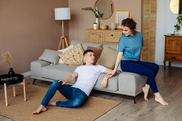 couple in home made clothes. sit on a warm wooden floor, spend time together with your beloved. A young guy at home sits on the floor,and looks at the girl. quarrel. Family relationships.