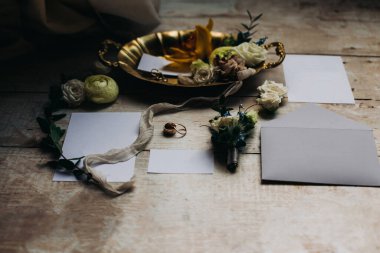 Çalışma alanı. Düğün detayları, davetiyeler, el işi zarfları, damat yaka çiçekleri, yüzükler, gelin mücevherleri, çiçekler, beyaz ahşap arka planda altın vazo. Yukarıdan bak. Güzel yerleşim