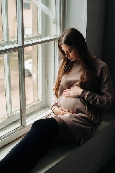 Okně Sedí Mladá Těhotná Evropanka Drží Ruce Břiše Podívá Dítě — Stock fotografie