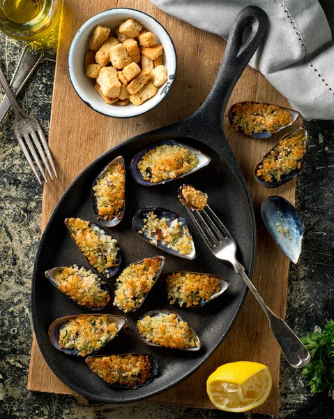 Delicious bakade musslor på en järn stekpanna med ströbröd, citron, persilja, vitlök och olivolja. — Stockfoto