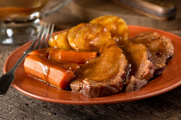 Un délicieux rôti maison avec pommes de terre, carottes et sauce . — Photo