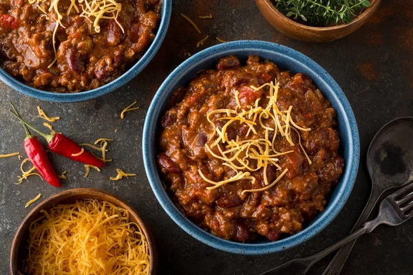 A bowl of delicious home made chili with ground beef, kidney beans, red pepper, tomato and shredded cheddar cheese. — Stock Photo, Image