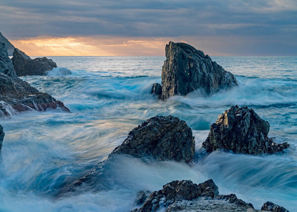 Sunrise landscape of ocean with waves clouds and rocks on beach