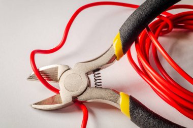 Gri arkaplanda kırmızı elektrik kablosunu kesen pense aracı