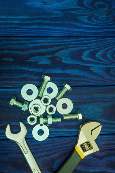 Adjustable spanner with metal nuts and bolts on blue vintage wooden background — Stock Photo, Image
