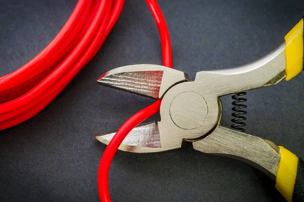 Szczypce narzędzie cięcia czerwony przewód elektryczny zbliżenie na czarnym tle — Zdjęcie stockowe