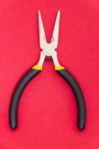 Egyedülálló fogó eszköz gumi fogantyúkkal a mester villanyszerelő a piros háttér — Stock Fotó