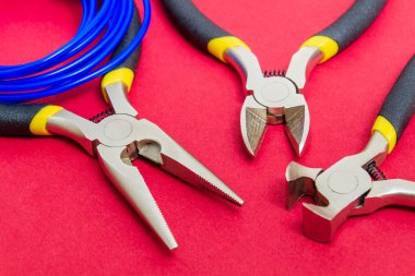 Kırmızı arkaplanda elektrikçi için pense aracı ve kablolar