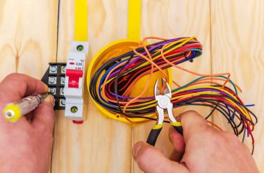 Usta elektrikçi kutudan penseyle kablo kesiyor.