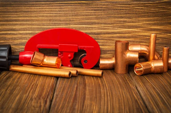 Red pipe cutter and copper pipes with connectors on vintage wooden boards