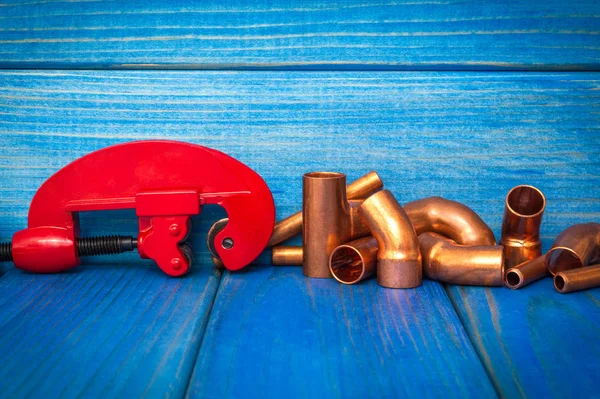 Red pipe cutter and copper pipes with connectors on blue wooden boards