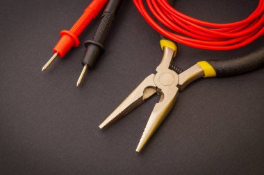 Elektrikçinin araçları ve kırmızı kablolar enerji verilmiş sistemleri veya iletişimi onarmak için siyah zemin üzerinde