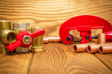 Kırmızı saplı yeni su topu vanası ve eski ahşap tahtalardaki su tesisatı tamiri için bakır borular.