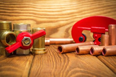 Kırmızı saplı yeni su topu vanası, pirinç tesisat ve eski ahşap tahtalardaki tesisat onarımı için bakır borular.