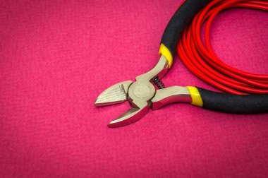 Kırmızı zemin üzerinde bir elektrikçi için pense aracı ve kablolar usta tarafından elektrik onarımında kullanılır