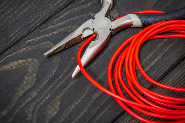 Electrician tool and red wire on black wooden boards for repairing energized systems or communications