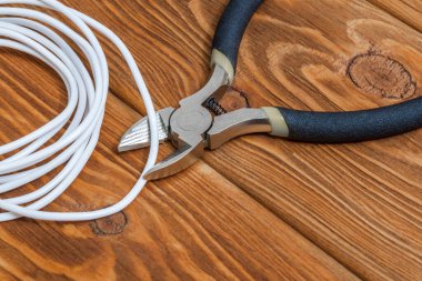 Elektrikli pense ve beyaz tel, elektrik sistemlerini ya da iletişimi onarmak için kullanılan eski ahşap tahtalar üzerinde.
