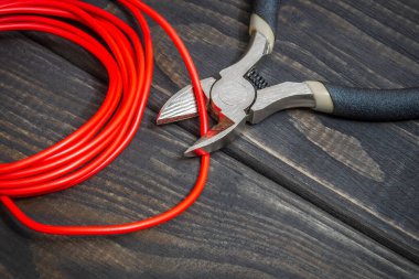 Elektrikçi pensesi ve kırmızı kablo, enerjili sistemleri ya da iletişimi onarmak için siyah tahta tahtalarda.