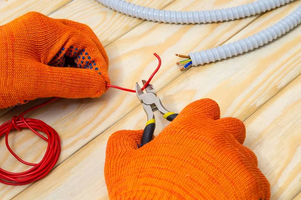 Master electrician with pliers cuts red wire on a working wooden table