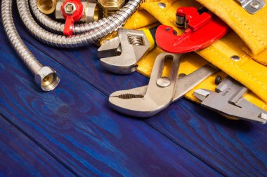 Sarı çantadaki tesisat araçları ve mavi tahta tahtalardaki yedek parçalar yenilenmek veya onarılmak için kullanılır