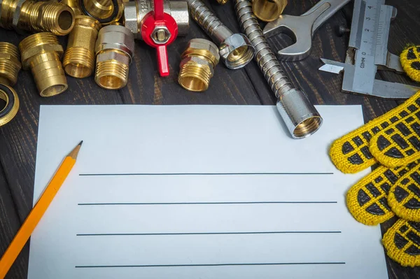 Drawing up plumbing repair plan with spare parts and tools on black wooden boards