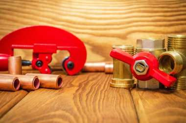 Kırmızı saplı yeni su topu vanası ve eski ahşap tahtalardaki su tesisatı tamiri için bakır borular.