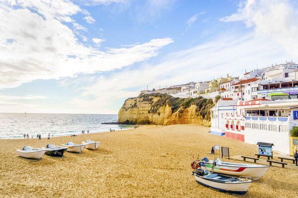Песчаный пляж с красочными лодками и скалами и белой архитектурой
