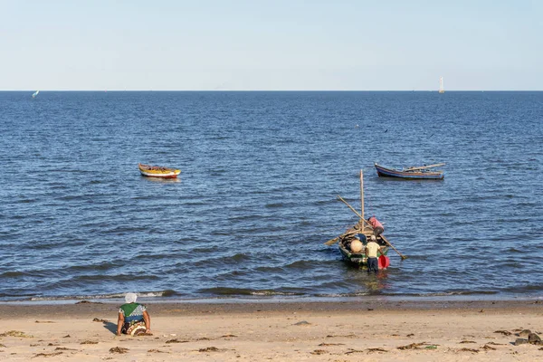 モザンビークのマプトのコスタ ソル海岸に座っている女性の間にボートで働く漁師 — ストック写真