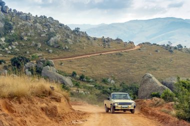 Eswatini 'nin muhteşem manzarasında kırmızı toprak yolda giden eski bir araba.
