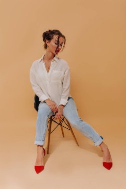 Toplanan saç ve kırmızı dudaklar izole bej arka plan üzerinde oturan oldukça şık kadın