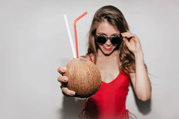 Uzavřete portrét stylové úžasné dámy s červeným plavením a brýle s červenými rty vytáhnete kokosový ořech do rámu — Stock fotografie