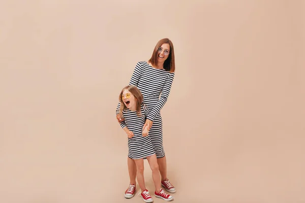 Madre con 6 años de edad hija con los mismos vestidos desnudos posando sobre fondo beige con emociones verdaderas felices — Foto de Stock