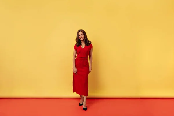 Полноразмерное фото очаровательная стильная привлекательная женщина с темными волосами в красном платье позирует на желтом и красном фоне — стоковое фото