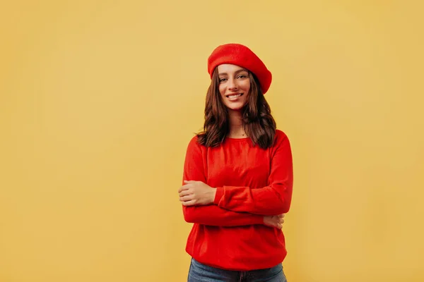 Чарівна усміхнена дівчина з темним волоссям у червоному береті та червоній блузці позує на жовтому тлі з посмішкою — стокове фото
