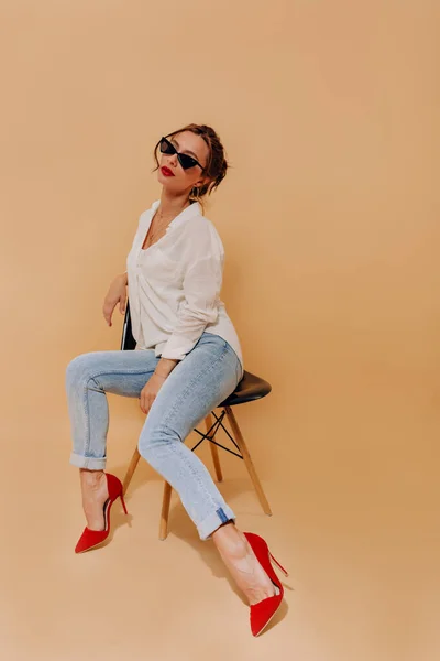 Mulher caucasiana elegante com cabelo escuro vestindo saltos vermelhos e camisa branca posando sobre fundo isolado com lábios vermelhos — Fotografia de Stock