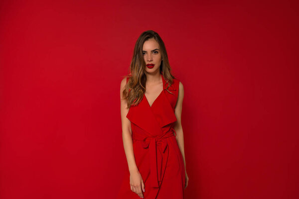 Elegant caucasian model wearing red dress standing with charming smile wearing evening dress.