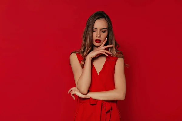 Романтическая стильная женщина в вечернем красном платье позирует на изолированном красном фоне во время фотосессии — стоковое фото
