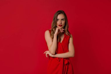 Kırmızı arka plan üzerinde duran zarif elbise inanılmaz ilgilenen kız. Kaygısız beyaz genç kadın gülümsüyor 