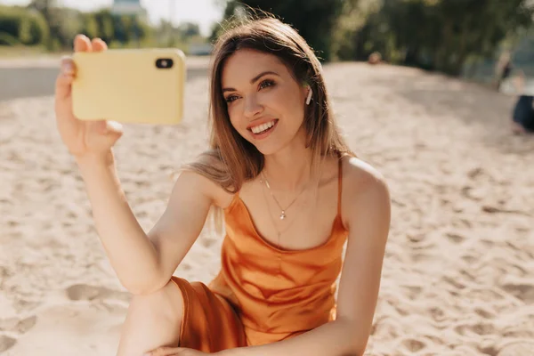 Charmante Europäerin mit schönem Lächeln in orangefarbenem Sommer-Outfit macht ein Selfie am Sommerstrand — Stockfoto