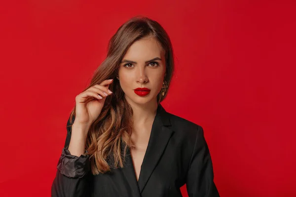Retrato de moda de mujer atractiva europea con pelo brillante y labios rojos mirando a la cámara sobre fondo rojo —  Fotos de Stock