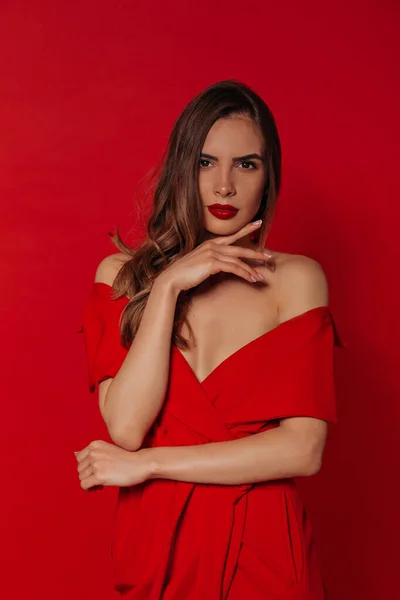 Wanita cantik modern yang percaya diri dengan bibir merah mengenakan gaun merah bergaya di atas latar belakang merah selama pemotretan — Stok Foto