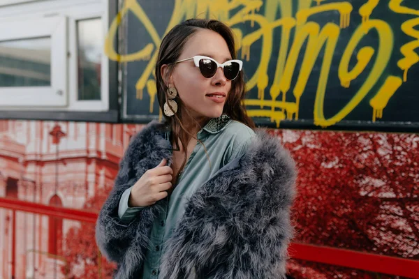 トレンディーな毛皮のコートと街の背景にポーズ金の宝石を持つ眼鏡でファッション魅力的な女性外の写真撮影中 — ストック写真