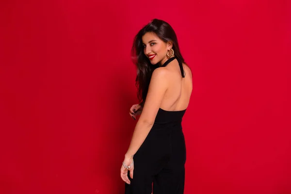 Estúdio retrato de elegante mulher encantadora vestindo vestido preto com nua de volta posando na câmera sobre fundo vermelho — Fotografia de Stock