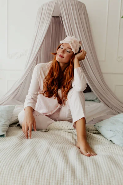 Uzun dalgalı kızıl saçlı, pijama ve uyku tulumu giyen hoş bir bayan. Sabah uyandığında evinde, yatakta uyanıyor.