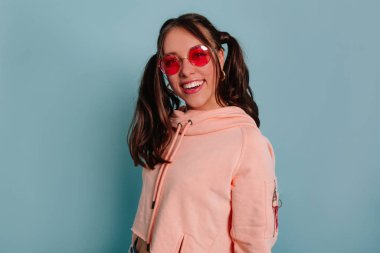 Mavi arka planda gülümseyen pembe bluzlu inanılmaz bir kızdan esinlendim. Beyaz tenli, neşeli kahverengi saçlı kızın stüdyo fotoğrafı. 
